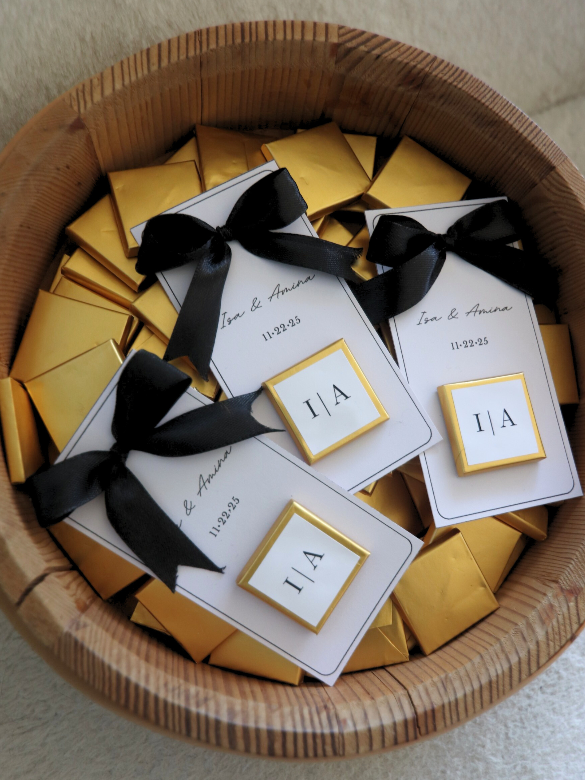 Basket filled with gold boxes and white cards with black ribbons, 3 wedding chocolate favours gold foil monogram in wooden basket