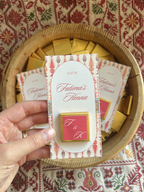 Henna chocolate favours with personalized design held by a hand, placed on a patterned tatreez fabric background.