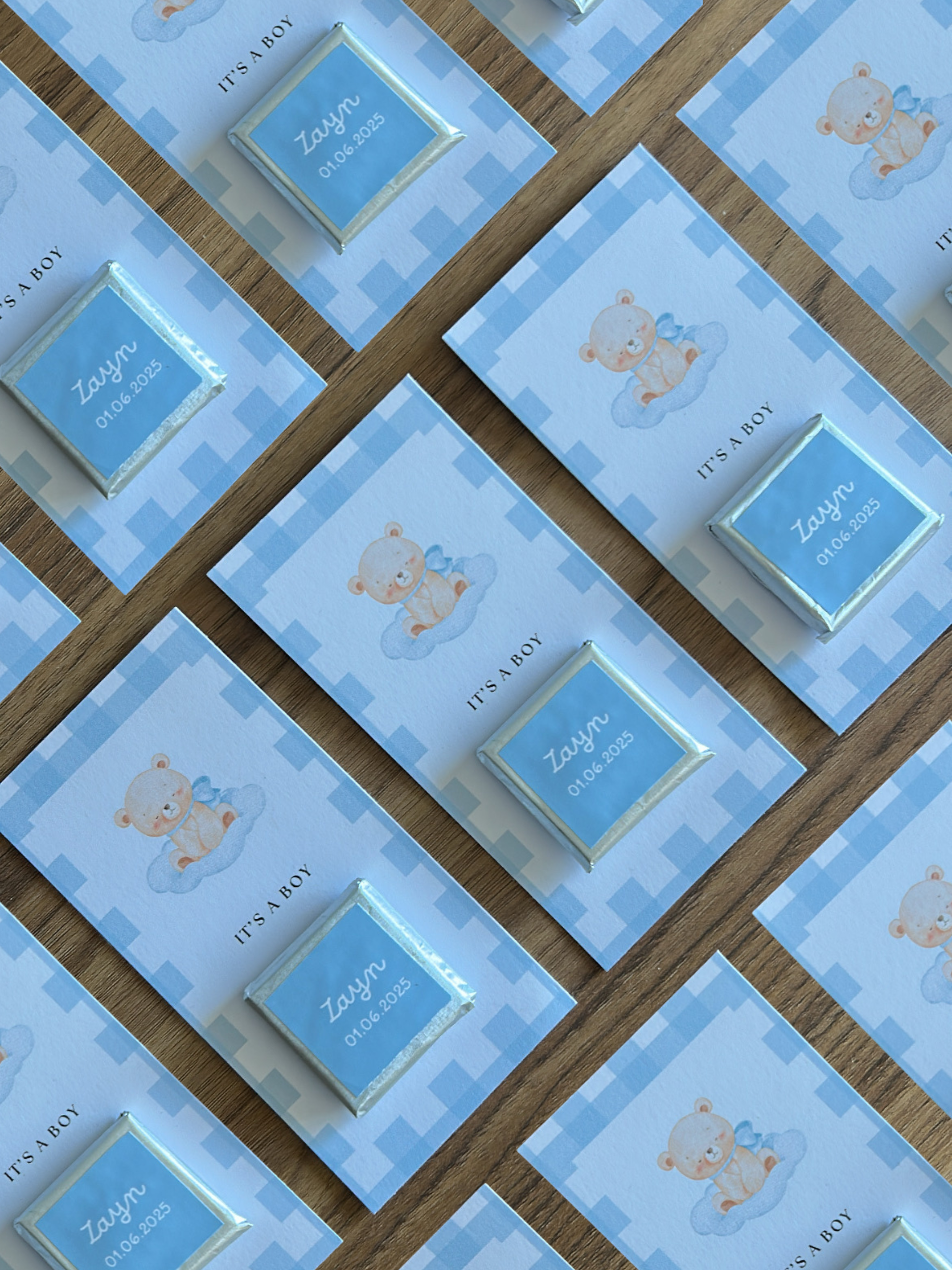 Collection of baby shower favor boxes with teddy bear design and 'It's a Boy' text on a wooden surface.
