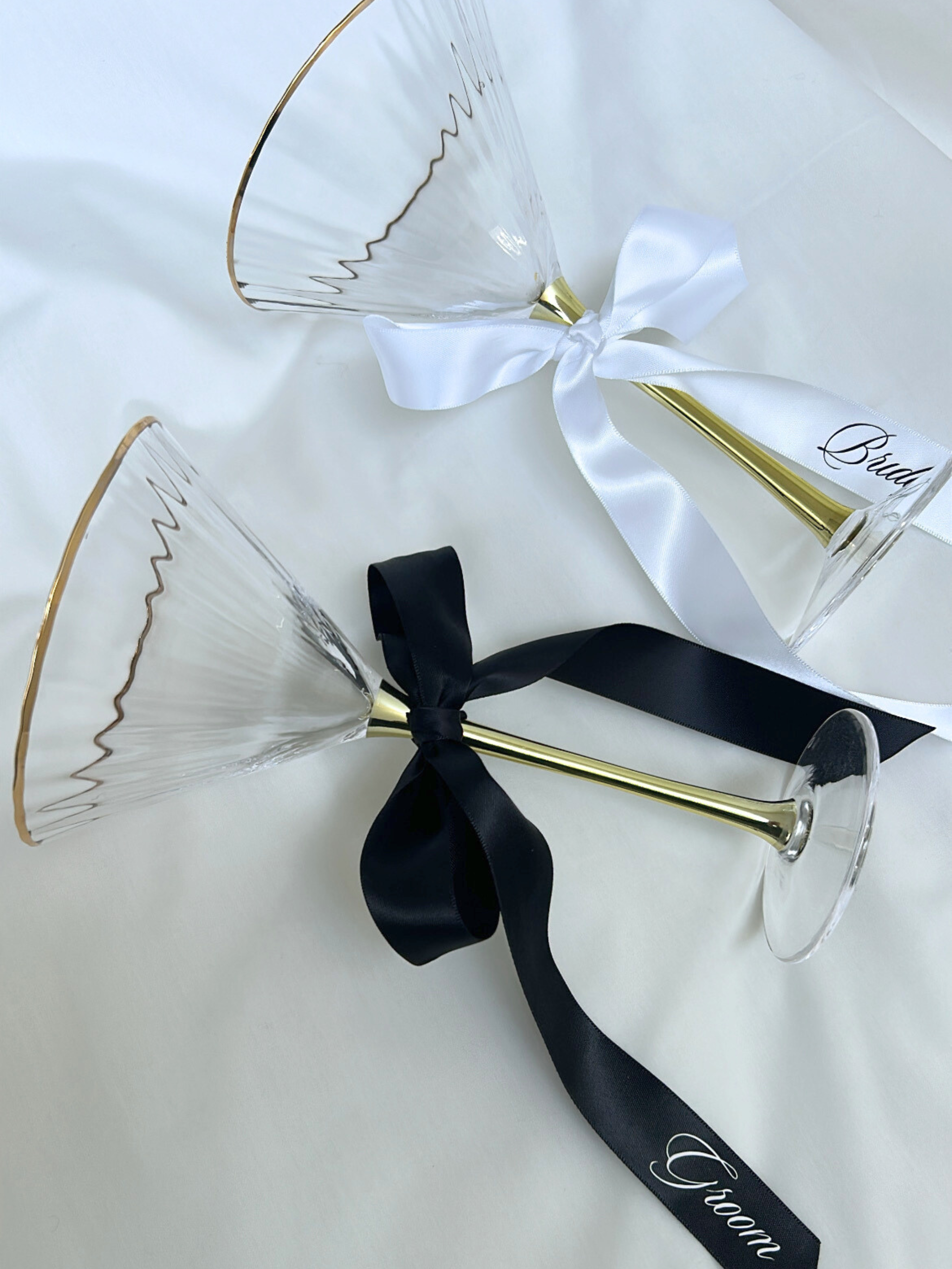 Two gold-rimmed glass flutes with black and white ribbons on a white background. bride and groom personalized custom wedding ribbons black and white