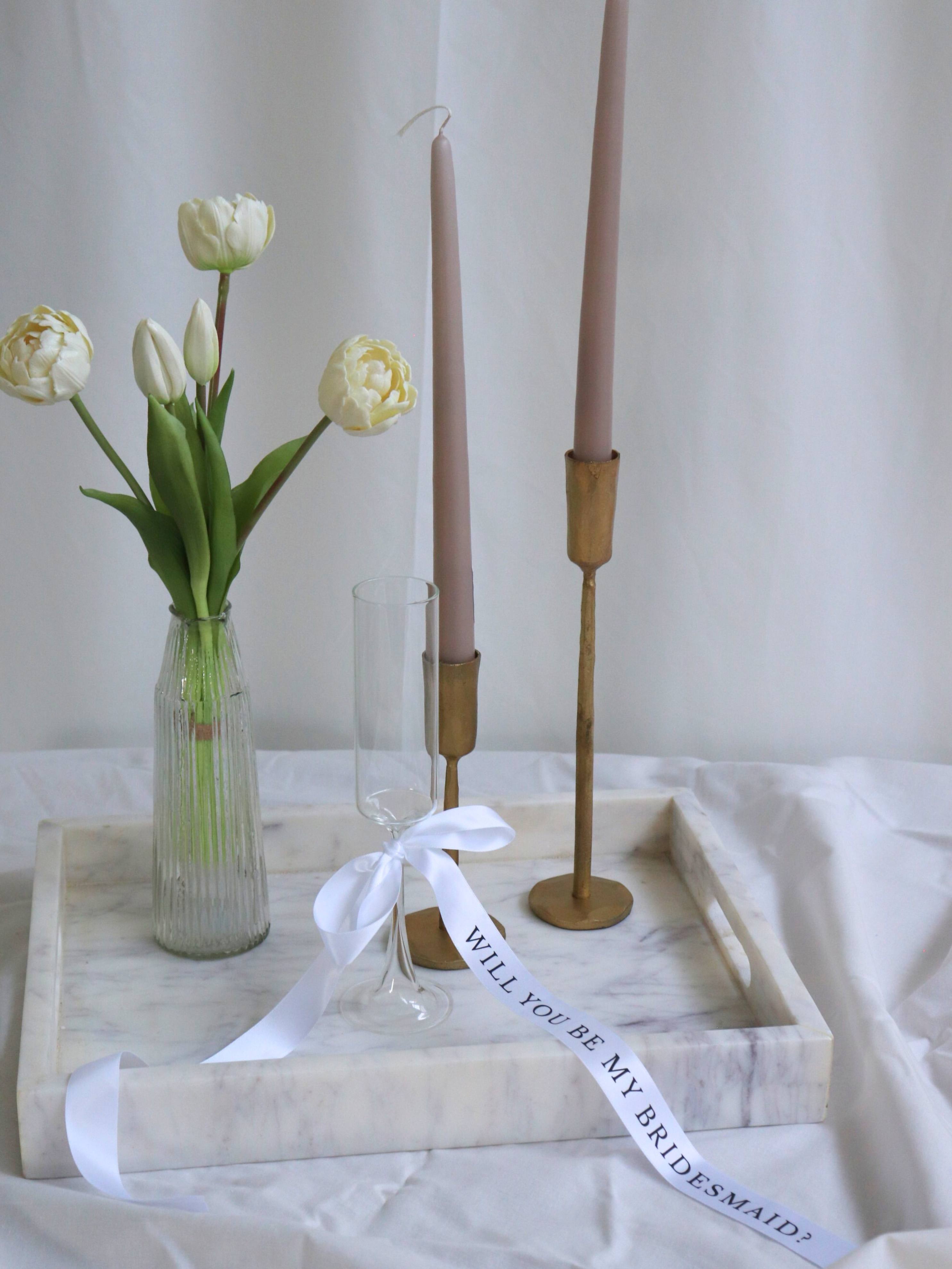 Decorative setup with candles, flowers, and a marble tray on a white surface. bridesmaid proposal ribbon white candle marble tray