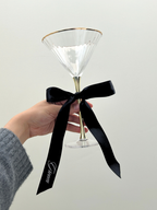 Clear cocktail glass with gold rim and black ribbon held by a hand against a white background. groom personalized custom wedding ribbons black and white