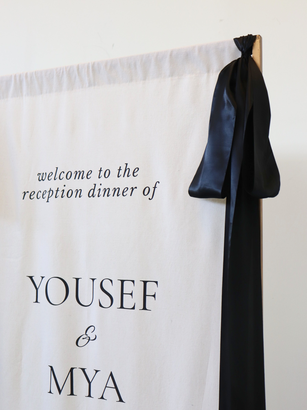Decorative backdrop with text 'welcome to the reception dinner of YOUSEF & MYA' and a black ribbon.