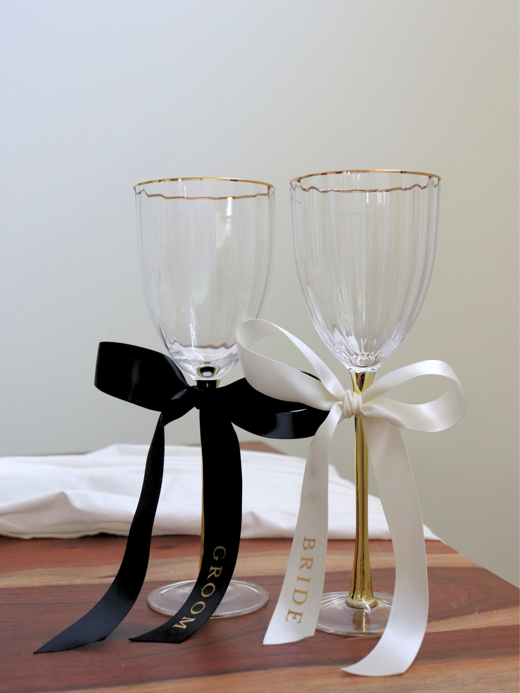 Two wine glasses with 'Bride' and 'Groom' ribbons on a wooden surface. wedding gold text bride and groom personalized custom wedding ribbons black and white on wood table