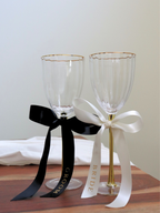 Two wine glasses with 'Bride' and 'Groom' ribbons on a wooden surface. wedding gold text bride and groom personalized custom wedding ribbons black and white on wood table
